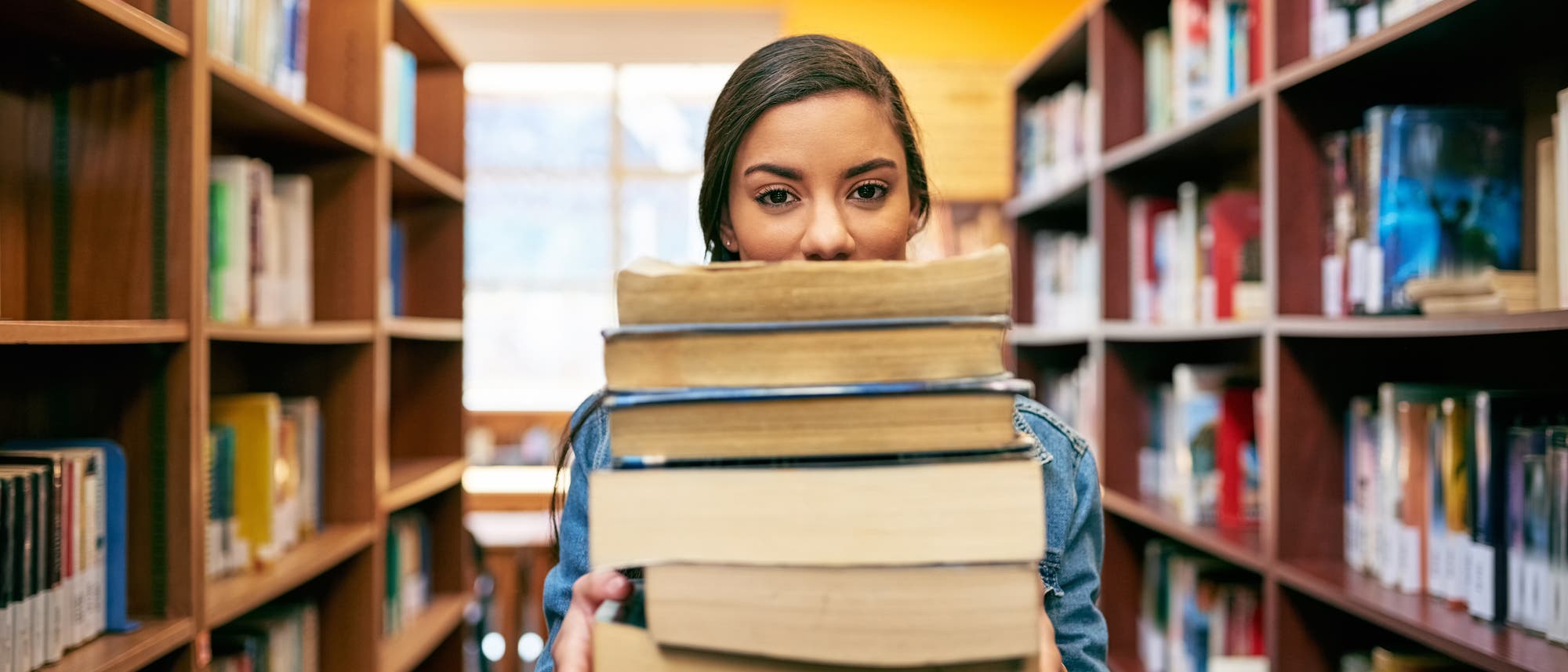 Frau h&auml;lt B&uuml;cherstapel in Bibliothek