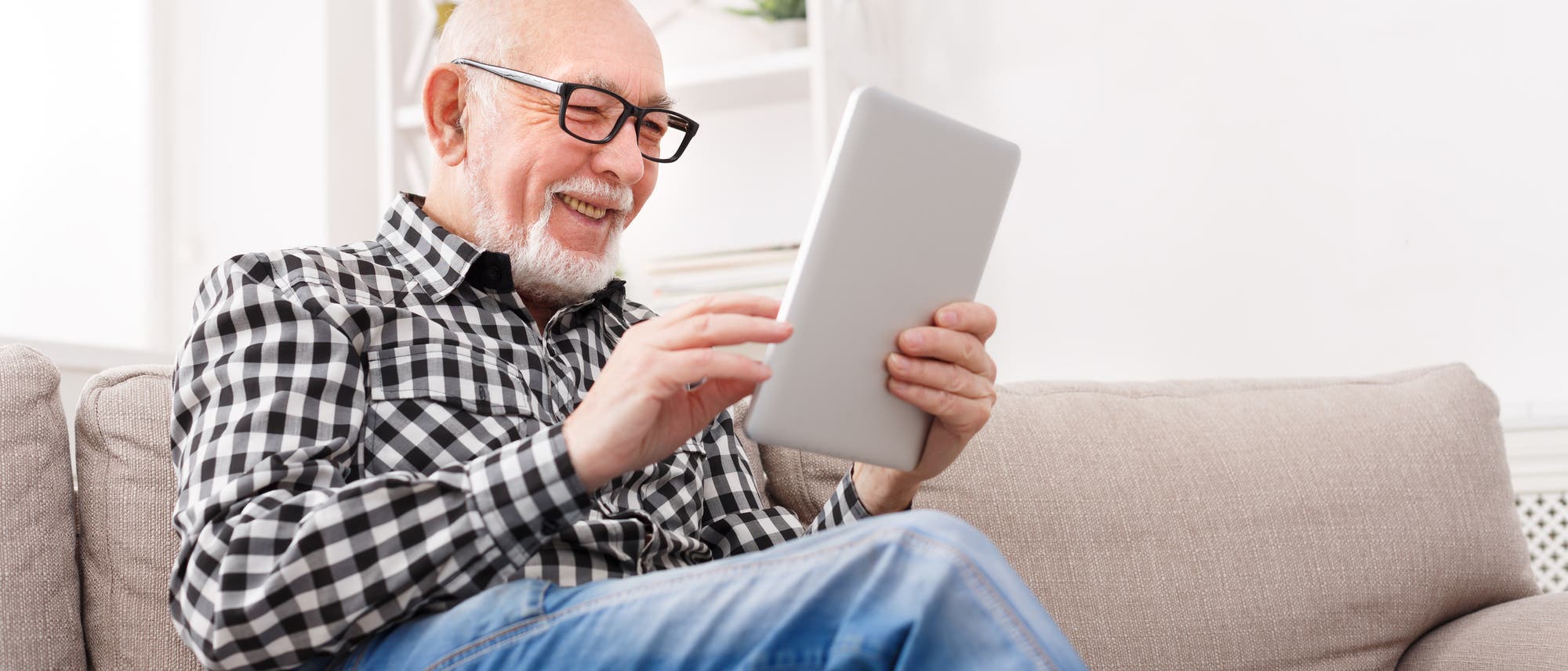 Älterer Mann guckt lächelnd auf sein Tablet.
