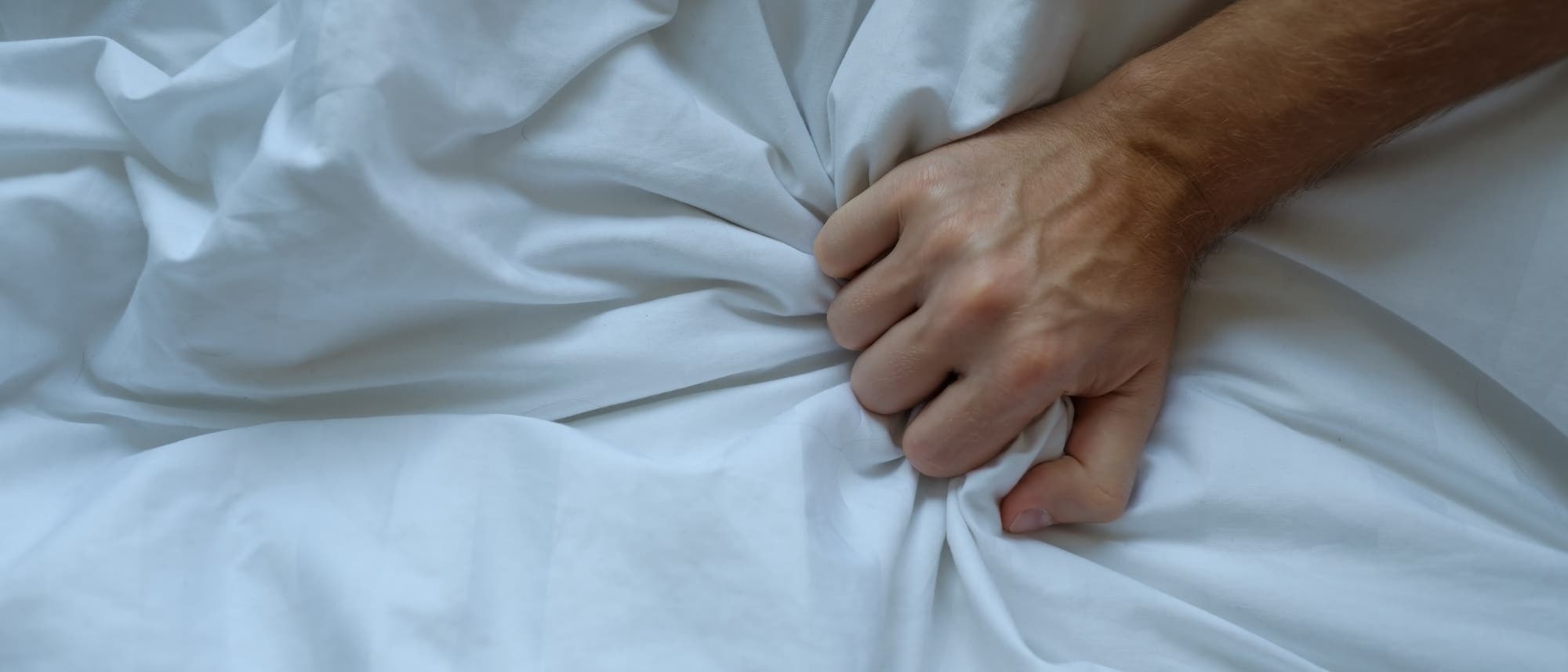 Männliche Hand krallt sich ins weiße Bettlaken