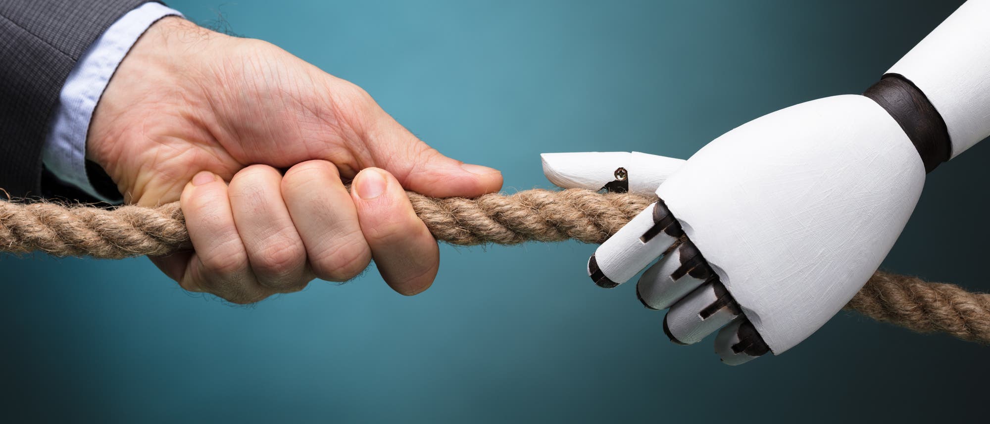 Eine menschliche und eine Roboter-Hand ziehen gegeneinander an einem Seil