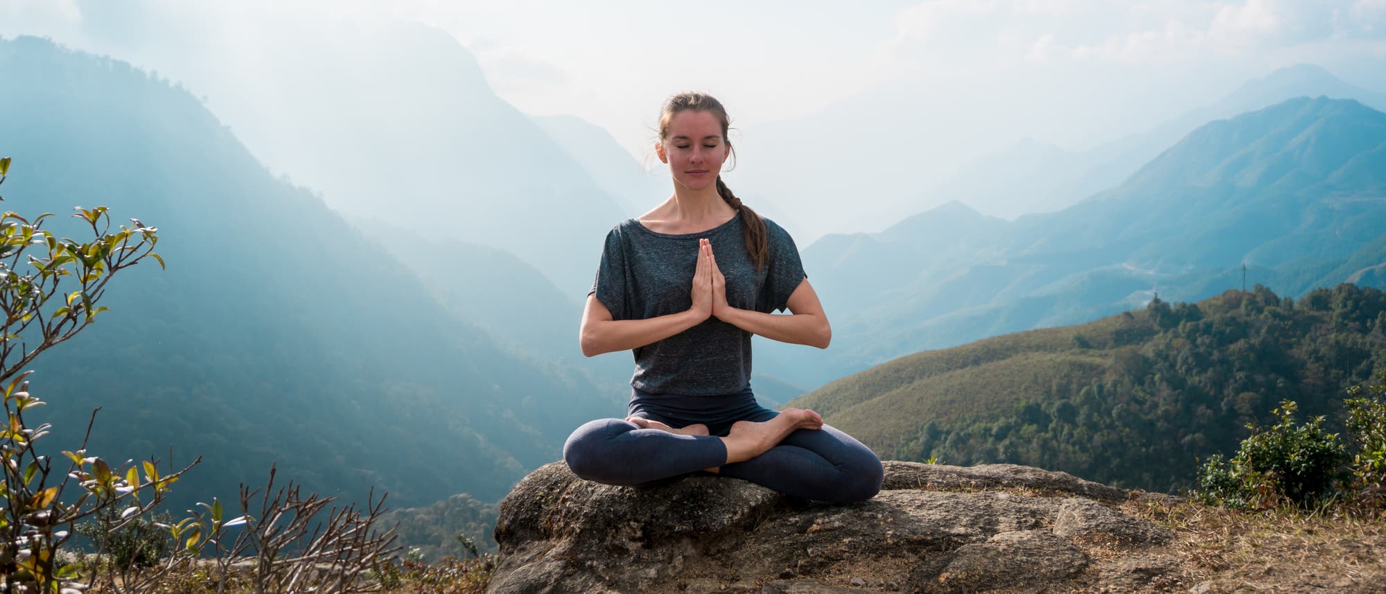Junge Frau im Yogasitz vor Bergpanorama