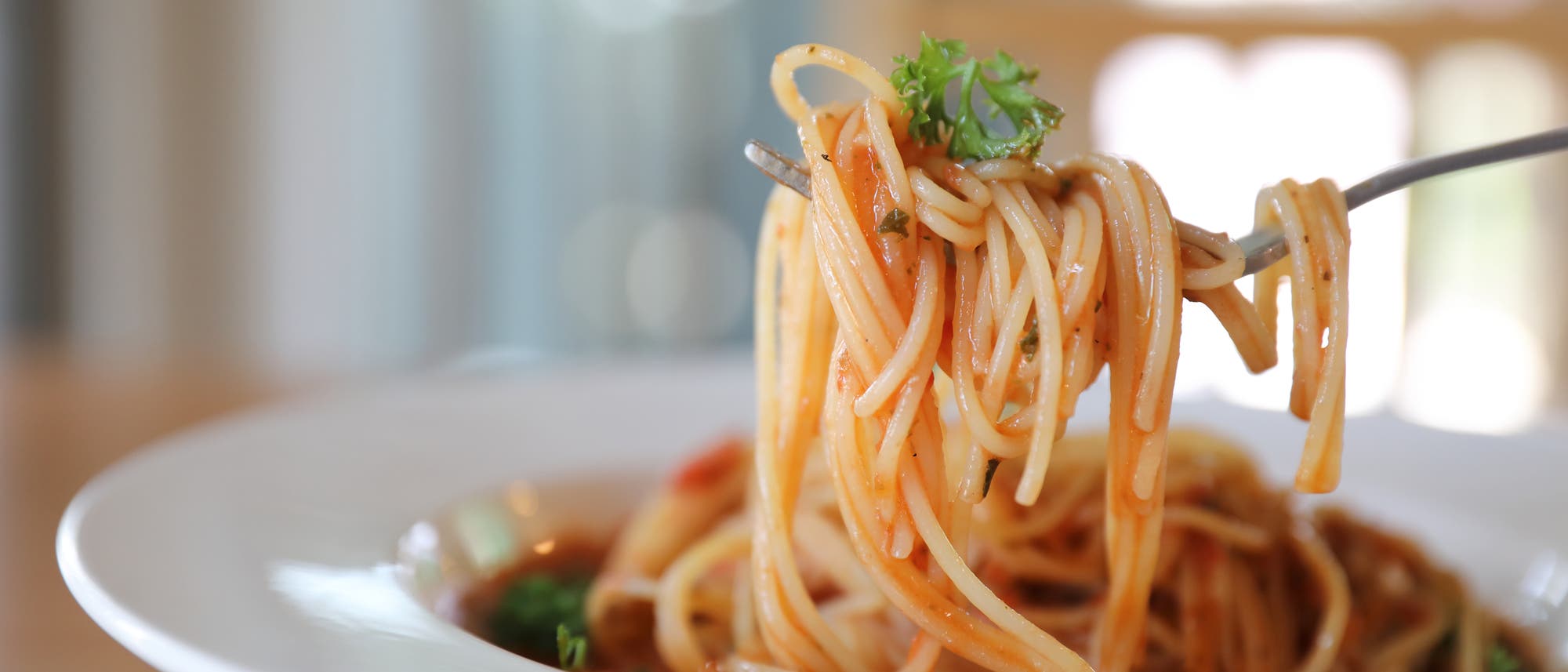 Eine mit Spagetti umwickelte Gabel schwebt über einem sehr vollen Teller mit Spaghetti bolognese. 