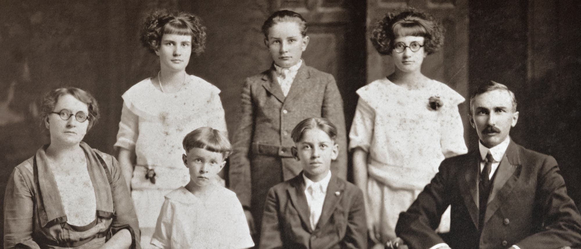 Historisches Schwarz-weiß-Foto einer Großfamilie. Rechts sitzt der Vater, links die Mutter. Dazwischen stehen und sitzen fünf Kinder verschiedenen Alters. Historisches Schwarz-weiß-Foto einer Großfamilie. Rechts sitzt der Vater, links die Mutter. Dazwischen stehen und sitzen fünf Kinder verschiedenen Alters.