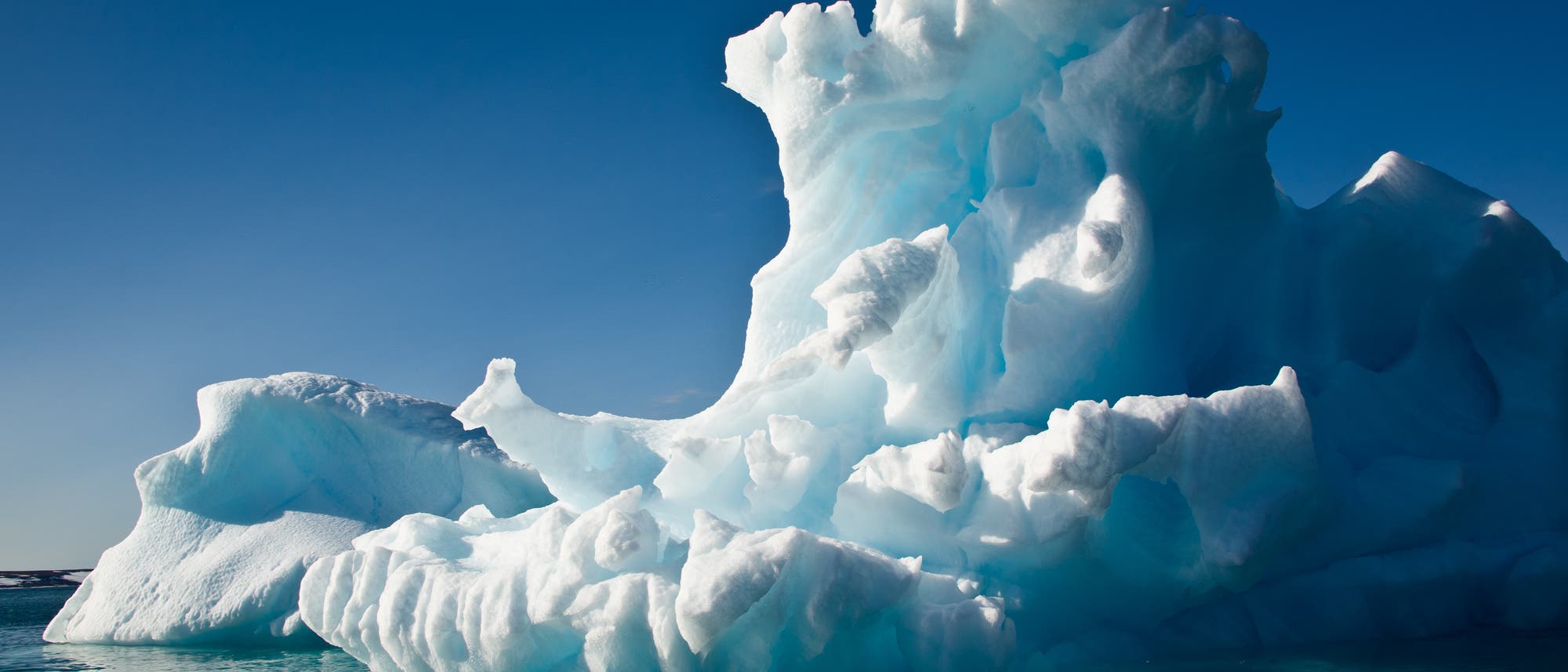 Ein mittelgroßer Eisberg schwimmt vor strahlend blauem Himmel bei Sonnenschein im Meer. Ein mittelgroßer Eisberg schwimmt vor strahlend blauem Himmel bei Sonnenschein im Meer.