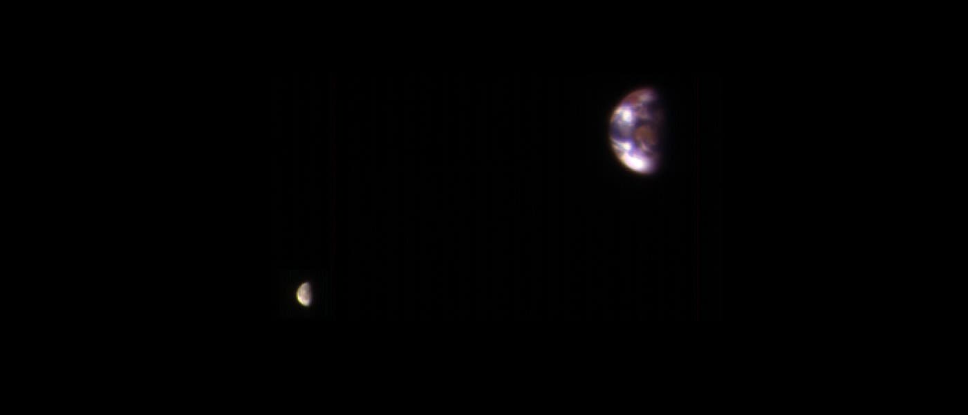Eine astronomische Aufnahme zeigt die Erde und den Mond im Weltraum. Die Erde erscheint rechts im Bild als gr&ouml;&szlig;erer, bl&auml;ulich-wei&szlig;er Planet mit sichtbaren Wolkenmustern. Links davon ist der Mond als kleinerer, grauer Himmelsk&ouml;rper zu sehen. Beide Objekte sind von einem tiefschwarzen Hintergrund umgeben, der den Weltraum darstellt.