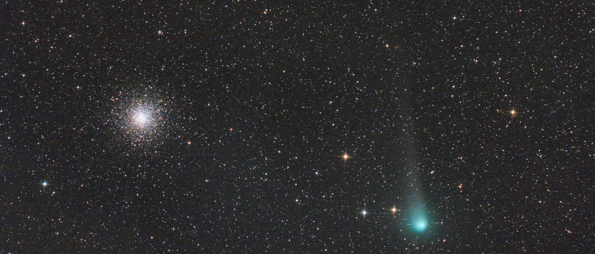 Ein astronomisches Bild zeigt einen dichten Sternenhaufen links und einen Kometen mit einem leuchtend gr&uuml;nen Schweif rechts. Der Hintergrund ist mit zahlreichen Sternen &uuml;bers&auml;t. Der Komet zieht einen langen, schmalen Schweif hinter sich her, der auf die Bewegung im Weltraum hinweist. Das Bild vermittelt die Weite und Vielfalt des Universums.