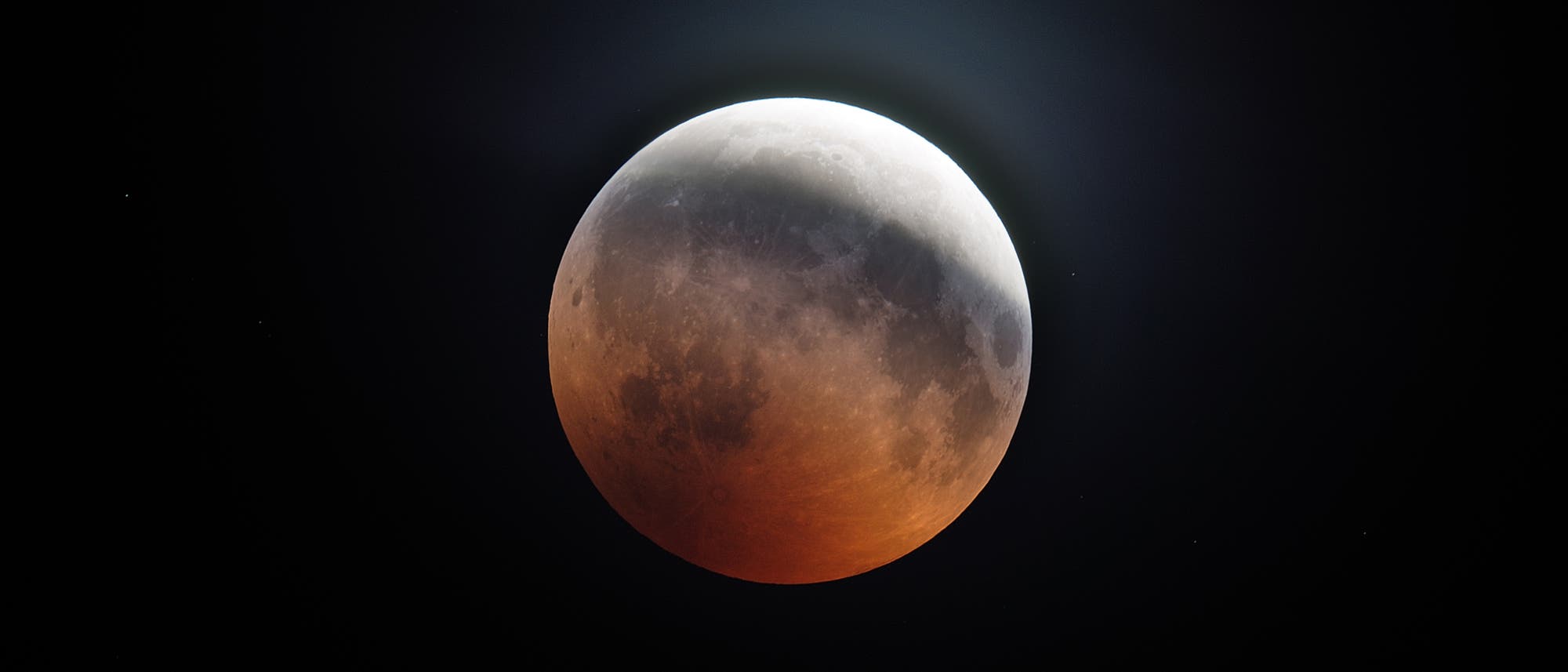 Das Bild zeigt eine totale Mondfinsternis, bei der der Mond in einem rötlichen Licht erscheint, umgeben von einem dunklen Nachthimmel. Der Schatten der Erde bedeckt den Mond teilweise, was zu einem eindrucksvollen Farbverlauf von Grau zu Rot führt. Diese Erscheinung wird oft als "Blutmond" bezeichnet. Im Hintergrund sind einige Sterne sichtbar. Das Bild zeigt eine totale Mondfinsternis, bei der der Mond in einem rötlichen Licht erscheint, umgeben von einem dunklen Nachthimmel. Der Schatten der Erde bedeckt den Mond teilweise, was zu einem eindrucksvollen Farbverlauf von Grau zu Rot führt. Diese Erscheinung wird oft als "Blutmond" bezeichnet. Im Hintergrund sind einige Sterne sichtbar.