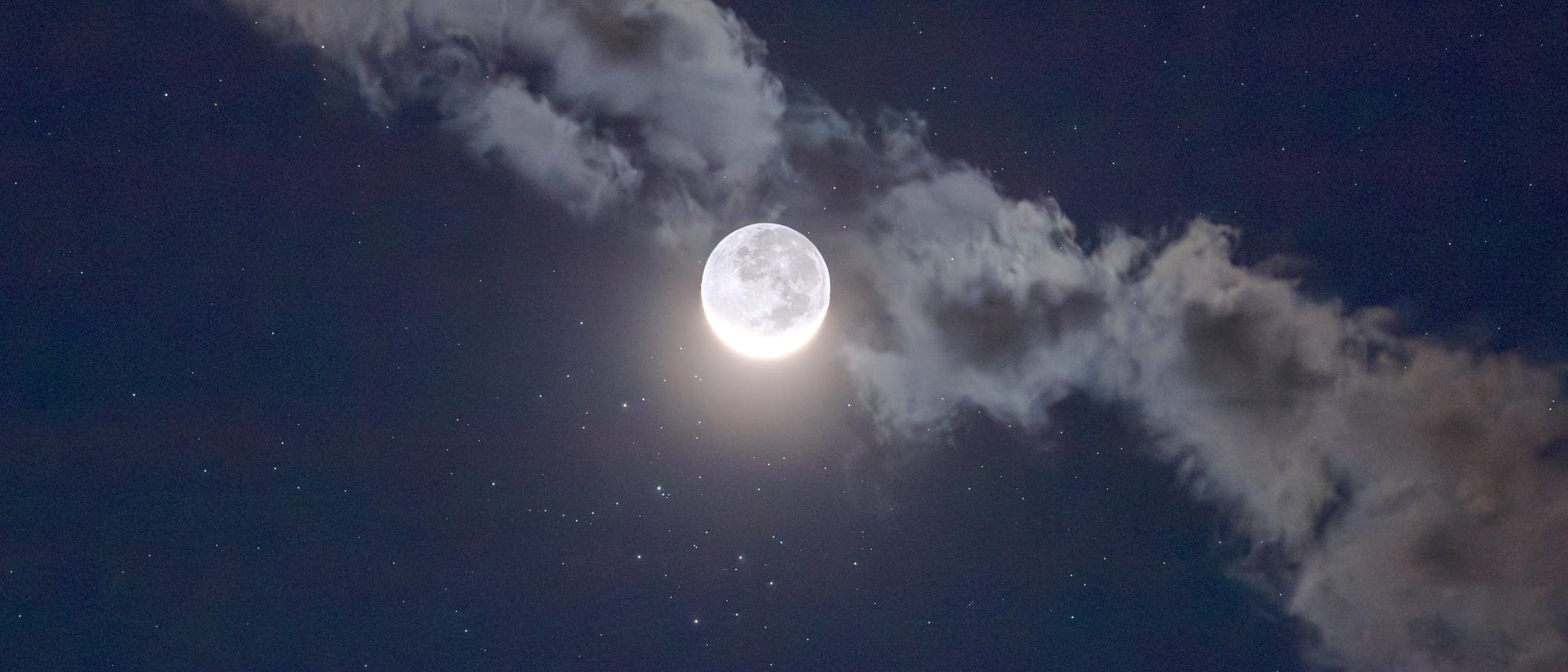 Ein Vollmond leuchtet hell am Nachthimmel, umgeben von einer dünnen Wolkenschicht, die diagonal durch das Bild verläuft. Zahlreiche Sterne sind sichtbar und verstärken die astronomische Szenerie. Der Mond strahlt ein sanftes Licht aus, das die Wolken leicht beleuchtet. Ein Vollmond leuchtet hell am Nachthimmel, umgeben von einer dünnen Wolkenschicht, die diagonal durch das Bild verläuft. Zahlreiche Sterne sind sichtbar und verstärken die astronomische Szenerie. Der Mond strahlt ein sanftes Licht aus, das die Wolken leicht beleuchtet.