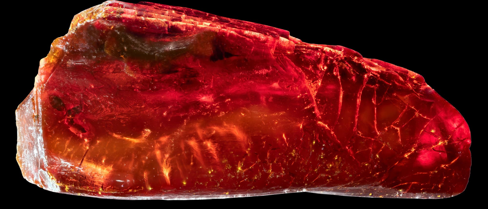 Ein leuchtend roter, transparenter Bernstein mit unregelmäßiger Form und glatter Oberfläche, die Licht reflektiert. Der Bernstein zeigt verschiedene Schattierungen von Rot und Orange, durchzogen von feinen Rissen und Einschlüssen. Der Hintergrund ist schwarz, was den Bernstein hervorhebt. Ein leuchtend roter, transparenter Bernstein mit unregelmäßiger Form und glatter Oberfläche, die Licht reflektiert. Der Bernstein zeigt verschiedene Schattierungen von Rot und Orange, durchzogen von feinen Rissen und Einschlüssen. Der Hintergrund ist schwarz, was den Bernstein hervorhebt.