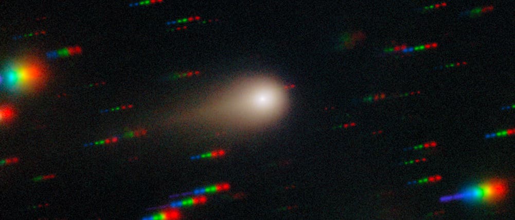 Ein astronomisches Bild zeigt einen Kometen mit einem leuchtenden Kern und einem diffusen Schweif, der sich nach rechts erstreckt. Um den Kometen herum sind bunte, spektrale Streifen zu sehen, die auf die Bewegung von Sternen oder anderen Himmelskörpern hinweisen. Der Hintergrund ist dunkel, was den Kontrast zu den hellen, farbigen Streifen und dem Kometen verstärkt. Das Bild vermittelt den Eindruck von Bewegung und Dynamik im Weltraum. Ein astronomisches Bild zeigt einen Kometen mit einem leuchtenden Kern und einem diffusen Schweif, der sich nach rechts erstreckt. Um den Kometen herum sind bunte, spektrale Streifen zu sehen, die auf die Bewegung von Sternen oder anderen Himmelskörpern hinweisen. Der Hintergrund ist dunkel, was den Kontrast zu den hellen, farbigen Streifen und dem Kometen verstärkt. Das Bild vermittelt den Eindruck von Bewegung und Dynamik im Weltraum.