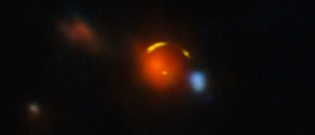 Ein astronomisches Bild zeigt eine Ansammlung von leuchtenden Objekten im Weltraum. Im Zentrum befindet sich eine helle, orangefarbene Galaxie, umgeben von einer gelben, bogenförmig verzerrten Hintergrundgalaxie, das einen Gravitationslinseneffekt darstellt. Mehrere kleinere, verschwommene Lichtpunkte sind im Hintergrund sichtbar, die möglicherweise entfernte Galaxien oder Sterne darstellen. Der dunkle Hintergrund hebt die leuchtenden Farben der Objekte hervor. Ein astronomisches Bild zeigt eine Ansammlung von leuchtenden Objekten im Weltraum. Im Zentrum befindet sich eine helle, orangefarbene Galaxie, umgeben von einer gelben, bogenförmig verzerrten Hintergrundgalaxie, das einen Gravitationslinseneffekt darstellt. Mehrere kleinere, verschwommene Lichtpunkte sind im Hintergrund sichtbar, die möglicherweise entfernte Galaxien oder Sterne darstellen. Der dunkle Hintergrund hebt die leuchtenden Farben der Objekte hervor.