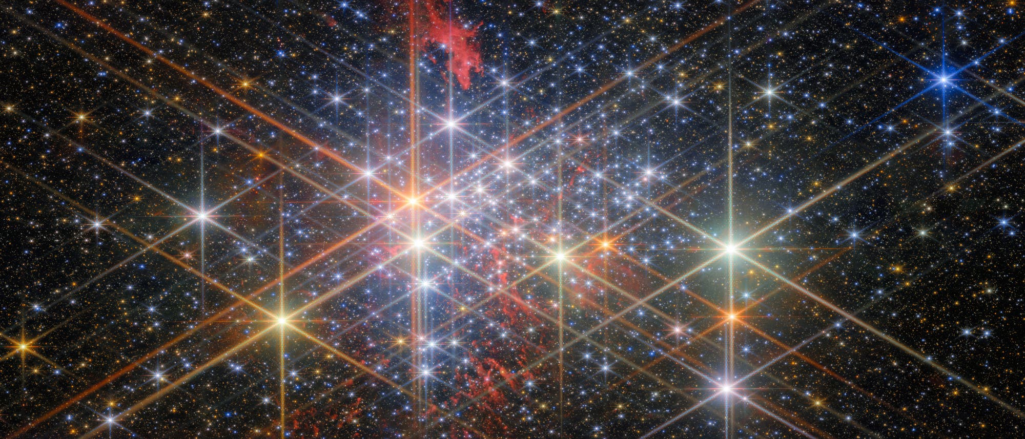 Ein dichtes Sternenfeld im Weltraum, das zahlreiche helle Sterne zeigt, die mit Lichtstrahlen hervorgehoben sind. Im Hintergrund sind unz&auml;hlige kleinere Sterne sichtbar, die den dunklen Himmel f&uuml;llen. In der Mitte des Bildes befindet sich ein roter Nebel, der sich durch das Sternenfeld zieht. Das Bild vermittelt die Weite und Sch&ouml;nheit des Universums und hebt die Vielfalt der kosmischen Objekte hervor.