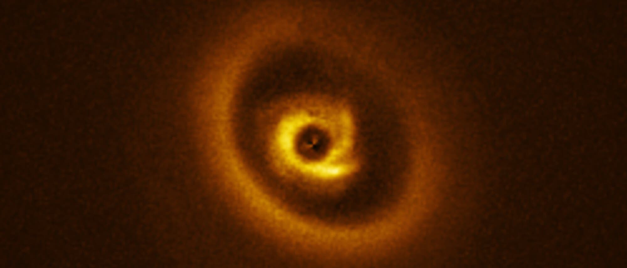 Ein leuchtender, spiralförmiger Protoplanetarer Nebel im Weltraum, der in warmen Gelbtönen auf einem dunklen Hintergrund leuchtet. Die Struktur zeigt mehrere konzentrische Ringe um einen zentralen Punkt. 