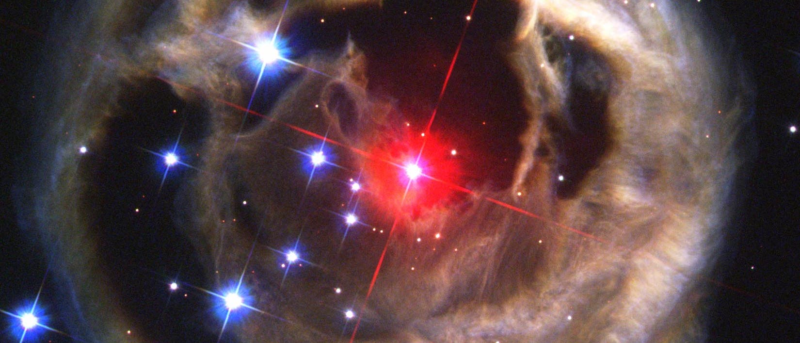 Im Zentrum der rot leuchtende Stern V838 Monocerotis, ringsherum ein konzentrischer Ring aus Lichtechos an Staubwolken.