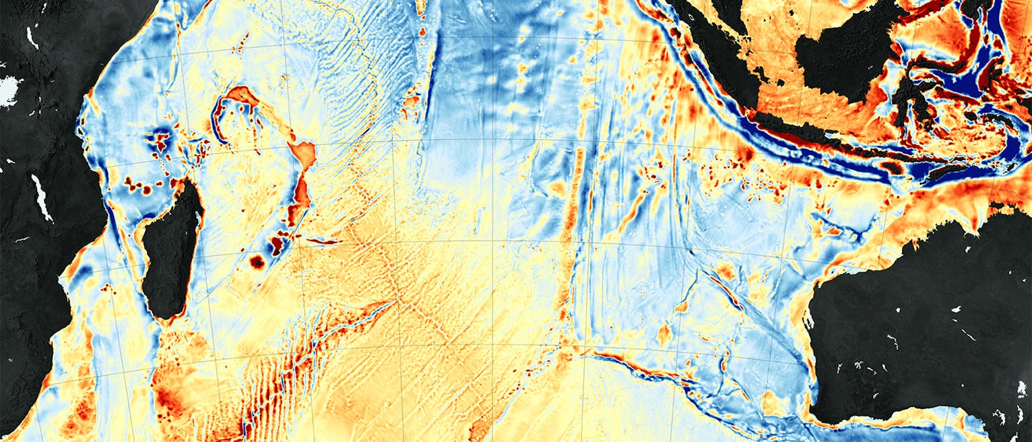 Karte des Bodens des Indischen Ozeans: Sie basiert auf Gravitationsdaten: Rot sind starke Abweichungen nach oben, dunkelblau nach unten. Gut erkennbar sind der Mittelozeanische Rücken links und der Ninetyeast Ridge rechts in der Karte, wo Vulkanismus dichtes Krustengestein erzeugt. In Schwarz sind Landmassen wie Madagaskar abgebildet.