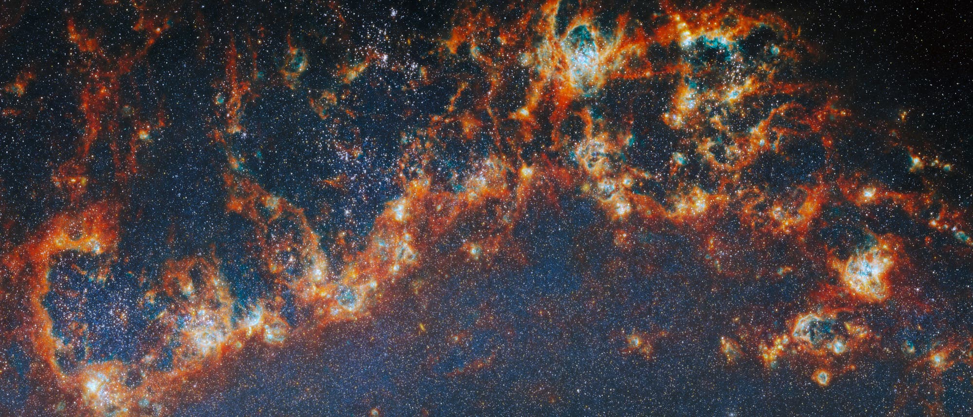 Das Bild zeigt eine detaillierte Aufnahme einer Galaxie mit leuchtenden Gaswolken und unz&auml;hligen Sternen. Die Farben reichen von tiefem Blau bis zu leuchtendem Orange und Rot, was auf verschiedene chemische Zusammensetzungen und Temperaturen hinweist. Die Struktur der Gaswolken ist komplex und filamentartig, was auf aktive Sternentstehungsprozesse hindeutet. Der Hintergrund ist mit vielen kleinen, funkelnden Sternen &uuml;bers&auml;t, die die Weite des Universums verdeutlichen.