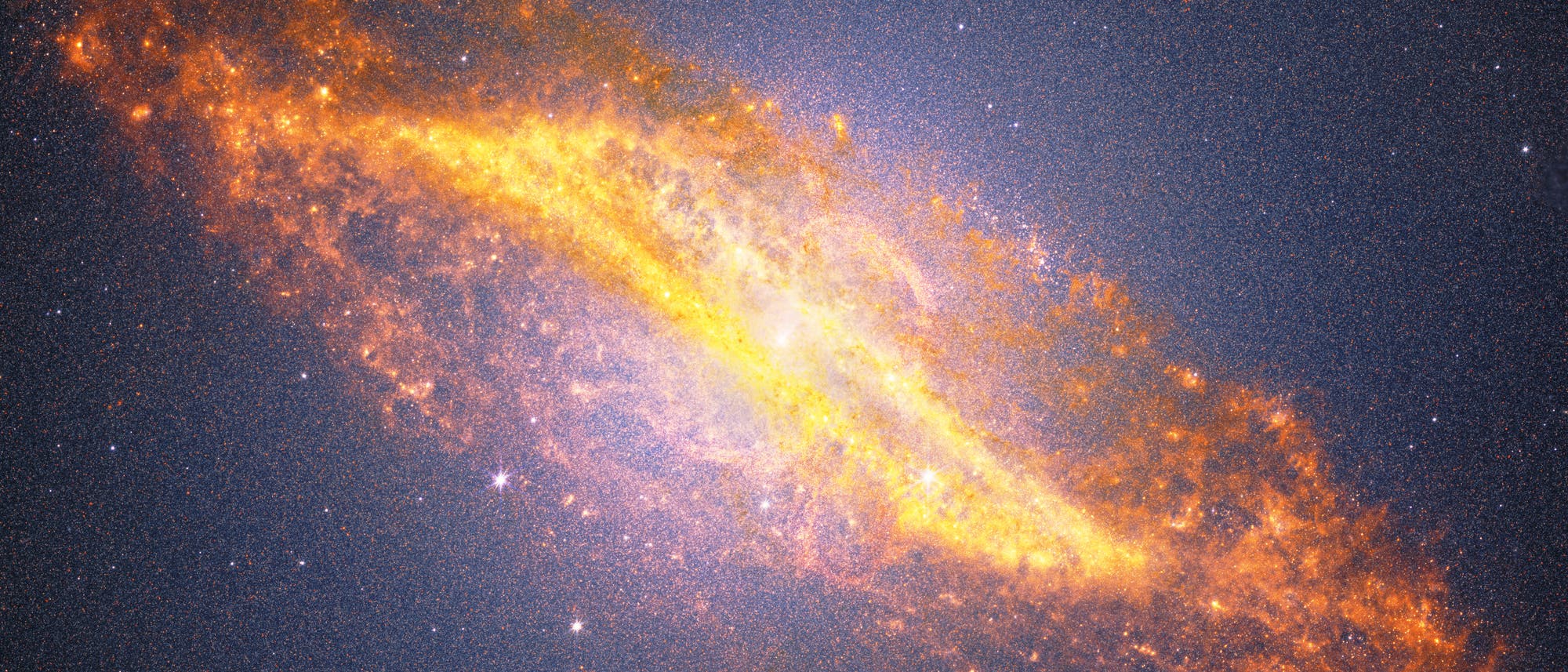 Eine farbenfrohe astronomische Aufnahme einer Spiralgalaxie, die sich diagonal durch das Bild erstreckt. Die Galaxie zeigt leuchtende, orangefarbene und gelbe Bereiche, die auf aktive Sternentstehung hinweisen, umgeben von einem dunklen, sternen&uuml;bers&auml;ten Hintergrund. Die Struktur der Galaxie ist deutlich sichtbar, mit einem hellen Zentrum und ausgedehnten Spiralarmen. Das Bild vermittelt die Weite und Sch&ouml;nheit des Universums.