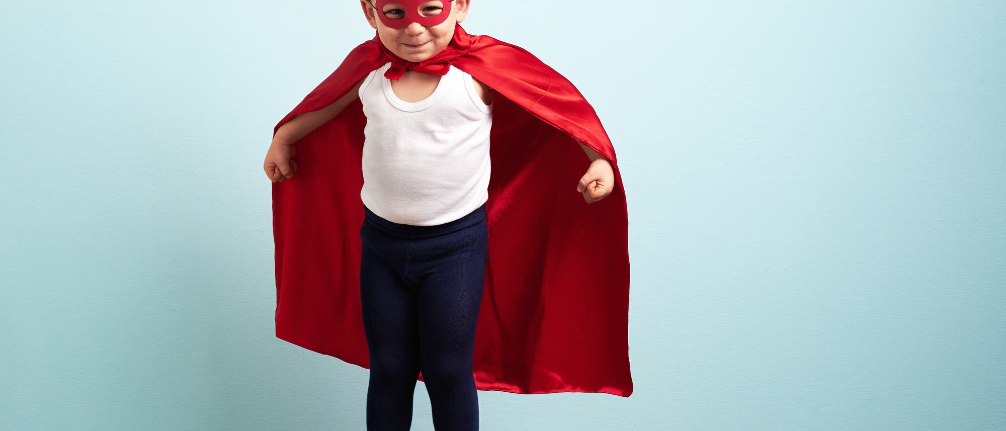 Ein Kind trägt eine Maske und ein rotes Cape. Es sieht aus wie ein Superheld.