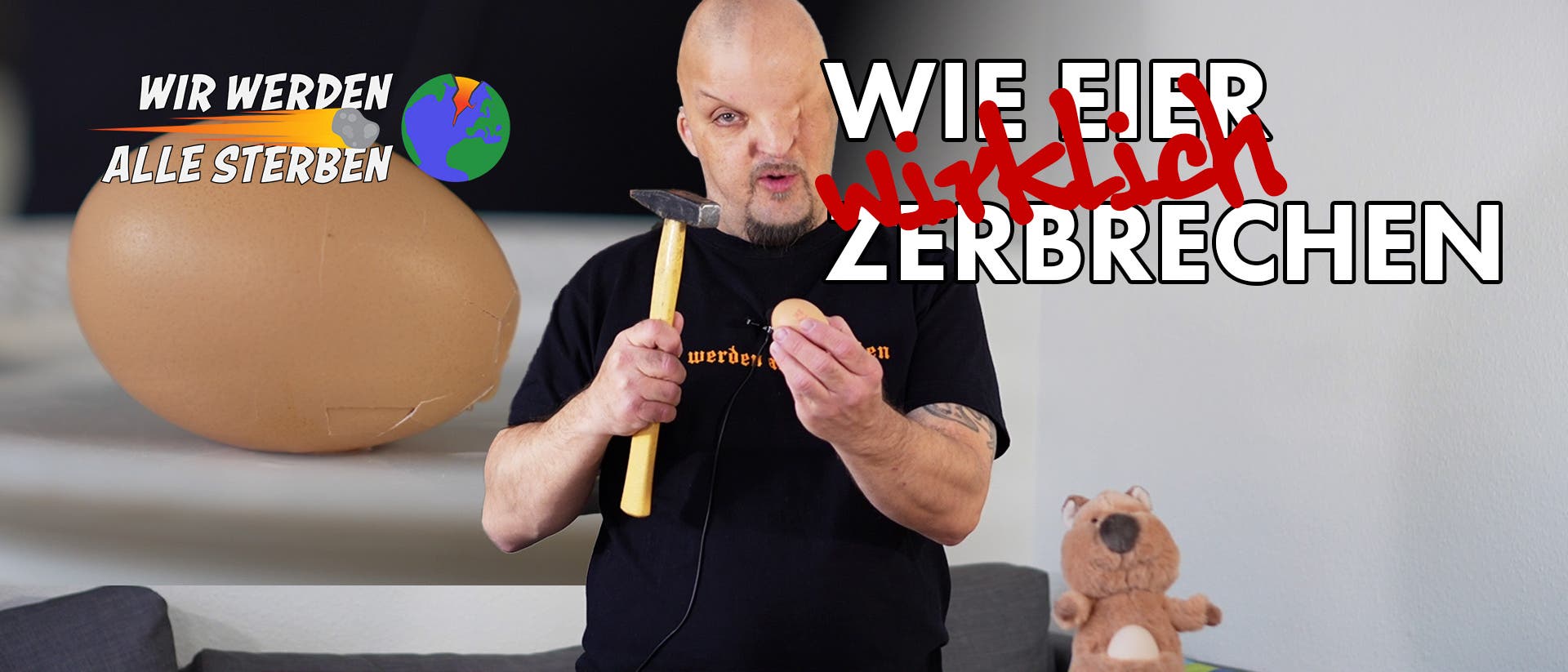 Eine Person steht vor einem Tisch und hält einen Hammer und ein Ei. Auf dem Tisch liegt ein leerer Teller. Links im Bild ist ein großes Ei mit der Aufschrift "WIR WERDEN ALLE STERBEN" und einer Weltkugel daneben. Rechts im Bild steht in großen Buchstaben "WIE EIER wirklich ZERBRECHEN". Ein Plüschtier steht ebenfalls auf dem Tisch. Die Szene vermittelt eine humorvolle Darstellung des Eierzerbrechens.