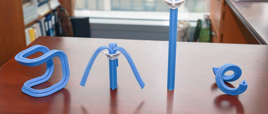 Ein Foto zeigt eine Tischplatte, auf der vier blaue, flexible Strukturen in Form der Buchstaben "S", "M", "I" und "L" angeordnet sind. Diese Strukturen bestehen aus einem modularen Material, das sich biegen und formen l&auml;sst. Im Hintergrund sind B&uuml;cherregale und ein Fenster zu sehen, was auf eine B&uuml;roumgebung hindeutet.
