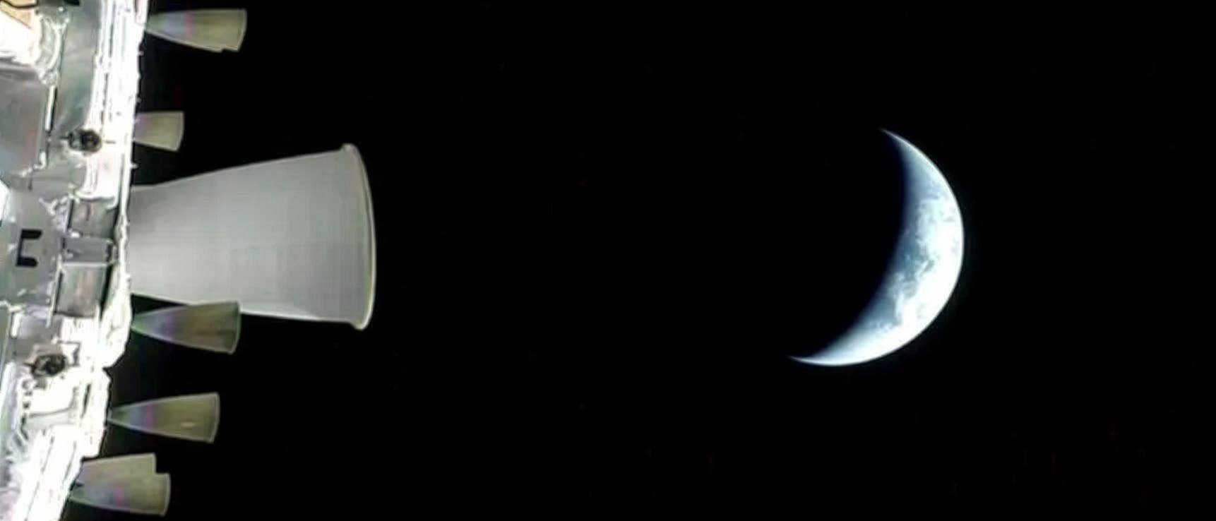 Ein Raumfahrzeug im Vordergrund links, mit mehreren D&uuml;sen sichtbar, schwebt im Weltraum. Rechts im Bild ist eine teilweise beleuchtete Erde zu sehen, die als Sichel erscheint. Der Hintergrund ist schwarz, was den Weltraum darstellt.