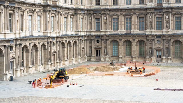 Ein historischer Innenhof mit aufwändiger Architektur, in dem Ausgrabungen stattfinden. Mehrere Arbeiter in orangefarbener Sicherheitskleidung sind um einen Bagger und Erdhaufen herum beschäftigt. Der Bereich ist mit orangefarbenen Sicherheitszäunen abgesperrt. Die Fassade des Gebäudes zeigt große Fenster und dekorative Details.