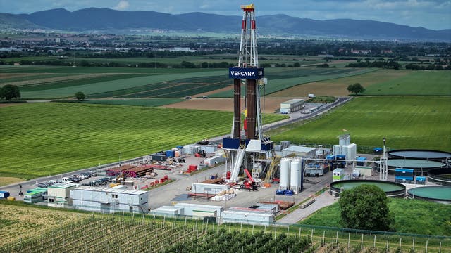 Eine Bohrplattform inmitten einer weitläufigen, grünen Landschaft mit Feldern und Hügeln im Hintergrund. Die Plattform ist von verschiedenen Containern und Tanks umgeben. Auf der Plattform ist der Schriftzug "VERCANA" zu sehen. Die Szene zeigt eine industrielle Anlage in einer ländlichen Umgebung unter einem bewölkten Himmel.