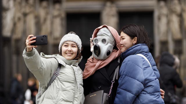 Touristen vor dem Kölner Dom posieren scherzhaft für ein Selfie mit einer Gasmaske am 29.02.2020.