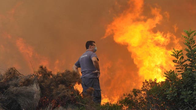 Ein Mann steht vor lodernden Flammen während eines Waldbrandes auf Rhodos