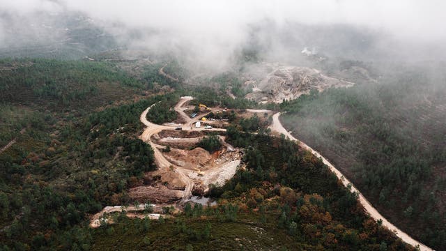 Eine Luftaufnahme zeigt eine Waldlandschaft, in deren Mitte eine Mine ausgebaggert wird.