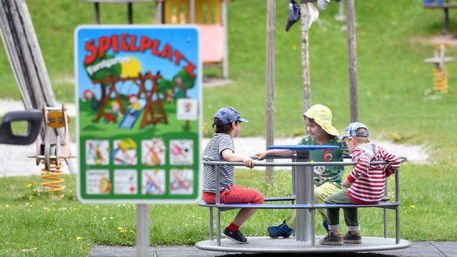Kinder sitzen auf einem Spielplatz in einem Karussel.