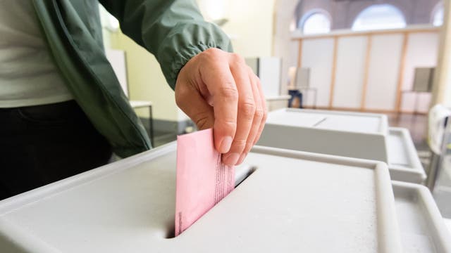 Eine Männerhand wirft einen rosa Umschlag in eine Wahlurne