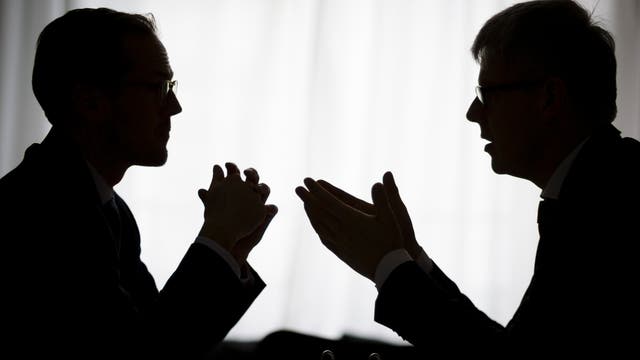 Silhouette zweier gestikulierender Männer im Gespräch vor hellem Hintergrund