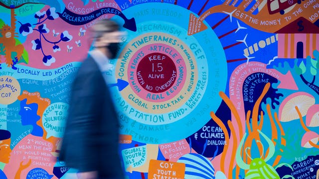 Ein Mann geht bei der UN-Klimakonferenz COP26 vor einem Wandbild zum 1,5-Grad-Ziel vobei. 