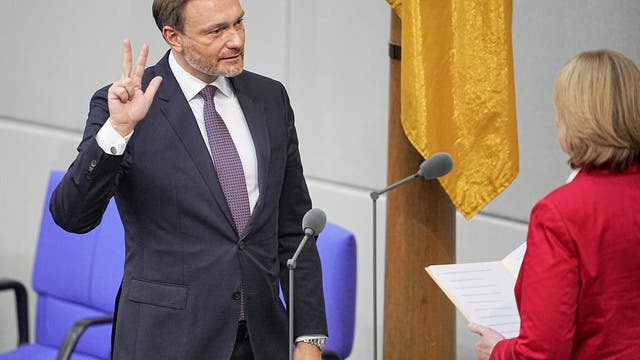 Der FDP-Politiker Christian Lindner steht im Plenarsaal des Deutschen Bundestags und hebt die rechte Hand, an der Daumen, Zeige- und Mittelfinger weggespreizt sind. Er trägt Anzug und Krawatte. 