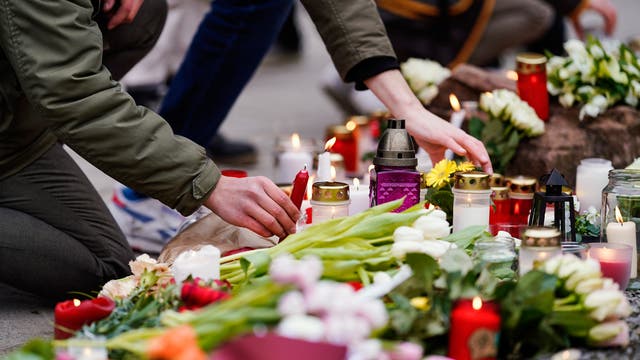 Menschen legen vor einem Gebäude der Universität Heidelberg Blumen und Kerzen an den Wegesrand