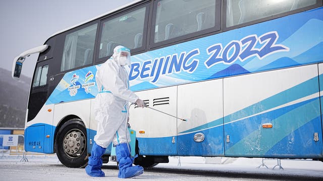 Ein Arbeiter in weißer Schutzkleidung desinfiziert einen Shuttlebus für die olympischen Spiele 2022.