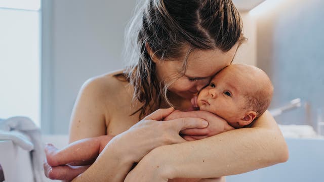 Eine Mutter sitzt in einer Badewanne und hält ihr Baby fest im Arm und kuschelt mit ihm