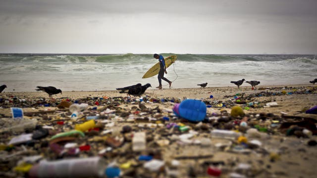 Ein Surfer steht am Strand vor einer Kulisse aus Müll