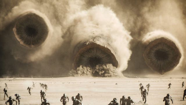 Filmszene: Sandwürmer pflügen durch den Sand auf eine Gruppe fliehender Menschen zu (aus Dune: Part 2)