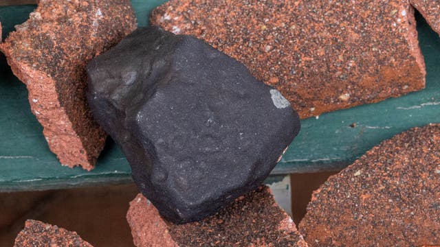 Ein schwarzes Stück Meteorit zwischen ein paar zerstörten, rotbraunen Dachziegeln.