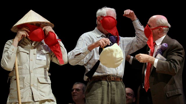 Roy Glauber, Sheldon Glashow und James Muller stehen bei der Verleihung der Ig-Nobelpreise auf der Bühne und halten sich BHs vor den Mund.