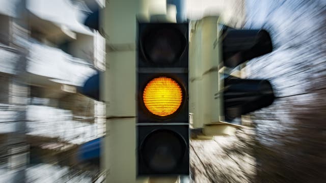 Eine Verkehrsampel mit gelbem Licht, das leuchtet, signalisiert den Fahrern, sich auf das Anhalten vorzubereiten. Die Umgebung ist verschwommen, was auf Bewegung oder Geschwindigkeit hindeutet.