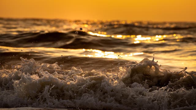 Dunkle Wellen branden im goldenen Abendlicht an den Strand
