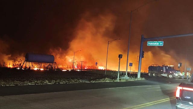 Waldbrand nahe einer Straße auf der Insel Maui, davor ein Feuerwehrauto bei Nacht