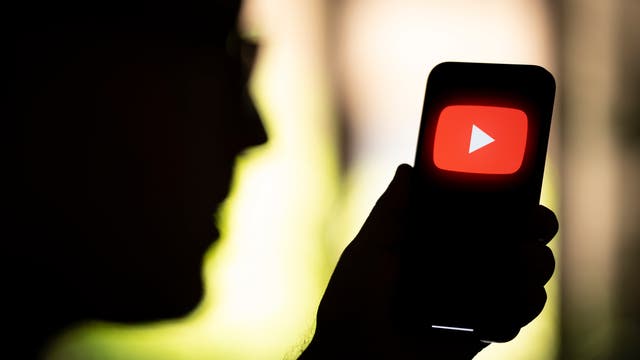 Ein Mann hält ein Smartphone in der Hand, auf dem das Logo von YouTube abgebildet ist.