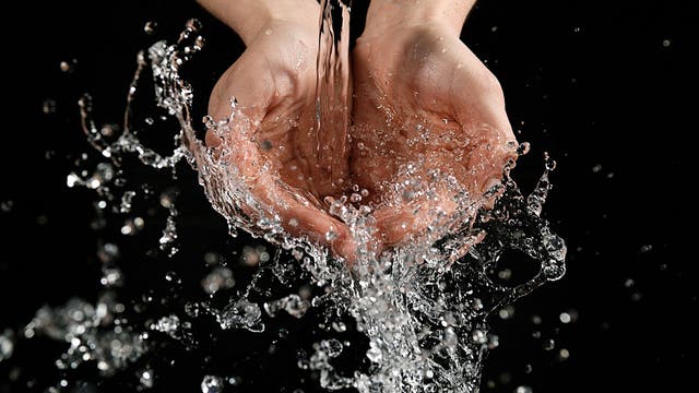 Hände vor schwarzem Hintergrund werden aus einem Wasserhahn mit Wasser begossen