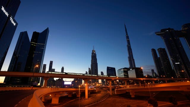 Skyline von Dubai bei Nacht, im Vordergrund fährt ein Zug