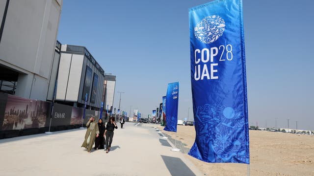 Menschen spazieren neben einer Fahne mit dem Logo der 28. Weltklimakonferenz in Dubai.