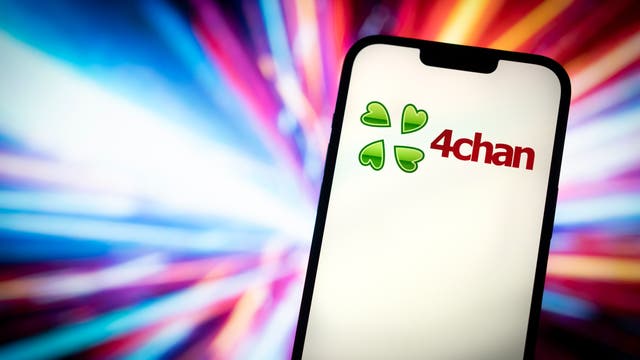 Ein Smartphone-Bildschirm zeigt das Logo von 4chan, bestehend aus einem grünen Kleeblatt-Symbol und dem Schriftzug "4chan" in roter Schrift. Der Hintergrund ist dynamisch und farbenfroh, mit verschwommenen Lichtstrahlen in Blau-, Rot- und Lilatönen, die eine energetische und lebendige Atmosphäre schaffen.